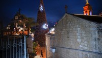 Seorang pria berjalan di dekat pohon Natal selama upacara penerangan, di luar Gereja Ortodoks Yunani Kabar Sukacita, di Nazareth, Israel, Minggu, (12/12/2021). (AP Photo/Oded Balilty)