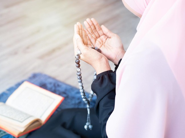 side of asian young beautiful muslim woman pray with beads and read quran sit on carpet mat with meditation in mosque.