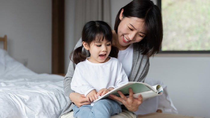 Young Asian mother is reading a book with her daughter