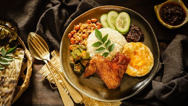 Nasi Lemak, the aromatic rice dish from Malaysia; also popular in Singapore. Fragrant rice cooked with coconut milk; accompanied with fried chicken, egg, peanut-anchovy, lady finger, cucumber and red chili sauce. This one-dish meal is plated on a luxurious ceramic plate.