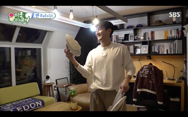 Di belakang kursi tempatnya bersantai, Siwon punya rak hitam yang dipenuhi koleksi buku, foto, dan beberapa topinya. Apartemennya memang tidak terlalu luas, namun dihiasi tanaman hijau di beberapa sudut yang membuat rumahnya terlihat asri. Foto: dok. SBS