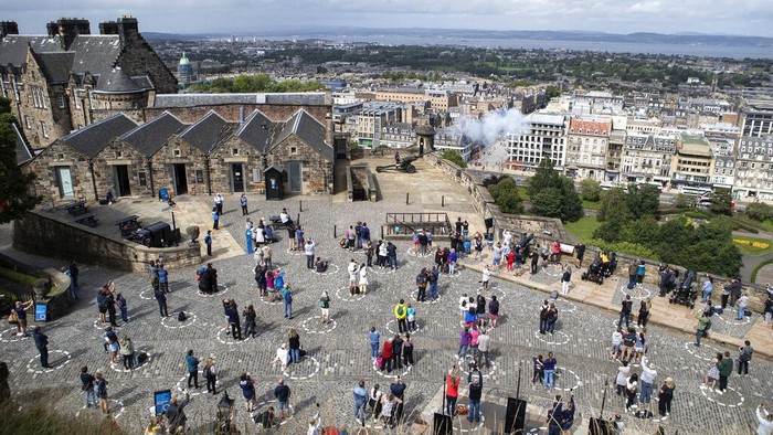 Kota-kota di Dunia yang Batalkan Perayaan Tahun Baru Gegara Omicron Pengunjung di Kastil Edinburgh berdiri dengan jarak sosial dalam lingkaran yang ditandai saat mereka menonton upacara senjata pukul satu setiap hari saat Skotlandia melanjutkan Fase 3 pembatasan penguncian virus corona, di Edinburgh, Skotlandia, Kamis, 20 Agustus 2020. (Jane Barlow/ PA melalui AP)