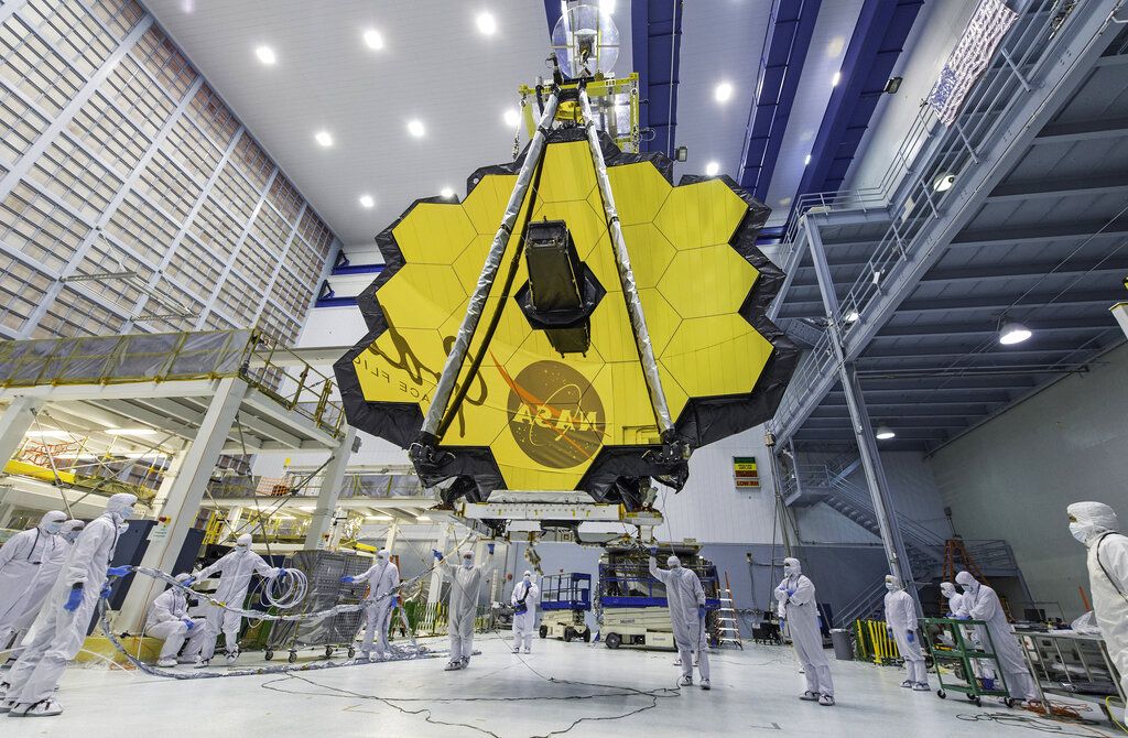 FILE - In this April 13, 2017 photo furnished by NASA, technicians lift the mirror of the James Webb Space Telescope using a crane at Goddard Space Flight Center in Greenbelt, Md.  NASA announced on Tuesday, December 14, 2021 that the launch of its new space telescope will be delayed by at least two days next week due to communication problems between the observatory and the rocket.  The James Webb Space Telescope is now expected to launch no earlier than December 24.  (Laura Betz/NASA via AP, File)