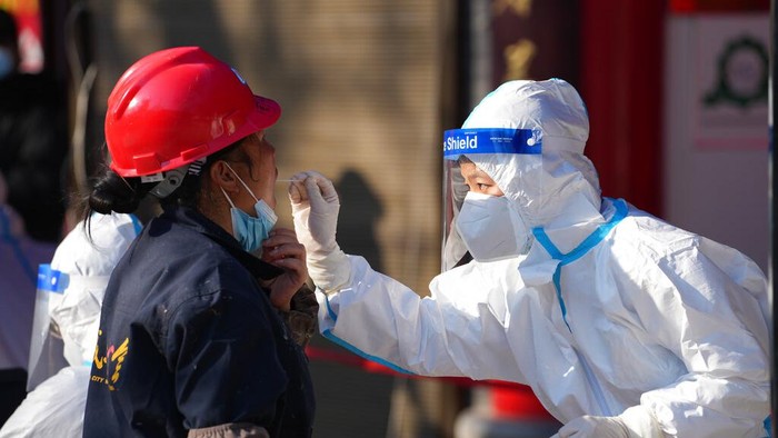 Dalam foto yang dirilis oleh Kantor Berita Xinhua China ini, seorang pekerja yang mengenakan pakaian pelindung mengumpulkan sampel usap tenggorokan di tempat pengujian COVID-19 di Xian di Provinsi Shaanxi, China barat laut, Selasa, 21 Desember 2021. China pada Rabu memerintahkan jutaan orang dikurung di lingkungan dan tempat kerja di kota utara Xian menyusul lonjakan kasus virus corona. (Li Yibo/Xinhua via AP)