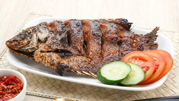 Honey Grilled Gurame, Grilled Gourami with honey and soy sauce. Served with chili sauce, cucumber and tomatoes on white plate. Close up and selective focus image.