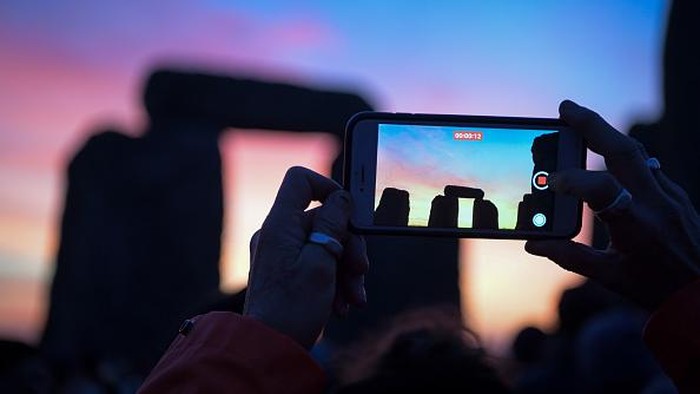 WILTSHIRE, ENGLAND - DECEMBER 22: Participants enjoy the sunset at Stonehenge on December 22, 2021 in Amesbury, United Kingdom. Along with the live stream, English Heritage, which manages the site, has allowed visitors into the event for the first time since the pandemic. The event is claimed to be more important in the pagan calendar than the summer solstice because it marks the 're-birth' of the Sun for the New Year. (Photo by Finnbarr Webster/Getty Images)