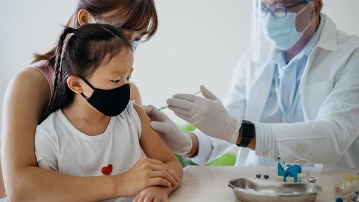 Image of a young asian girl getting a vaccine injection on her arm from a healthcare worker. Woman accompanying her daughter to get a vaccine injection at medical clinic.