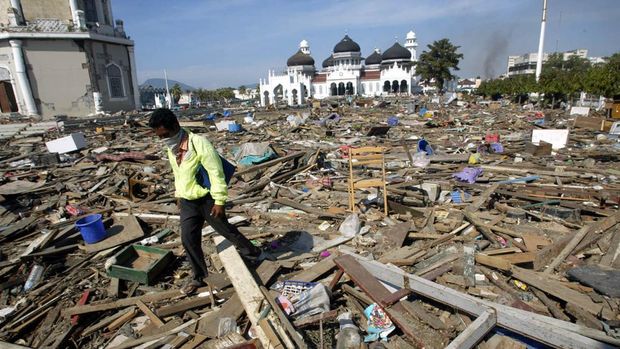 FILE - In this Dec. 29, 2004 file photo, an Acehnese man walks through debris near the Baiturrahman Grand Mosque in Banda Aceh, about 240 kilometers (150 miles) from the earthquake's epicenter, Indonesia. When the powerful tsunami smashed into this Indonesian city ten years ago, the only structures left standing in many neighborhoods were mosques. For the hundreds who found refuge within their walls, the buildings lifesaving role has not been forgotten - and for many, that experience strengthened their faith. Architectural experts say the mosques in Banda Aceh survived because they were sturdily built and had stronger foundations than surrounding structures, many of which were likely constructed of shoddier materials. But many survivors believe the mosques were spared by divine intervention. (AP Photo/Dita Alangkara, File)