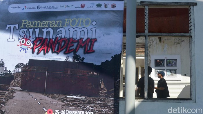 Pengunjung menyaksikan pameran foto bertajuk Tsunami Pandemi di situs tsunami Kapal Atas Rumah, Desa Lampulo, Banda Aceh, Aceh, Sabtu (25/12/2021). Organisasi profesi nirlaba Pewarta Foto Indonesia (PFI) Aceh menggelar pameran foto dengan tema Tsunami Pandemi Siaga Bencana Tangguh Bersama melawan COVID-19 dalam rangka peringatan 17 tahun Tsunami Aceh 26 Desember 2021. ANTARA FOTO/Ampelsa/wsj.