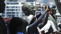 Orang-orang mengambil foto di patung Uskup Agung Anglikan Desmond Tutu di V&A Waterfront di Cape Town, Afrika Selatan, (26/12/2021). Pada 1984, Desmond Tutu diberi Hadiah Nobel Perdamaian atas usahanya melawan apartheid. Pada 1986, dia diangkat sebagai Uskup Agung dan menggunakan posisinya untuk mengadvokasi sanksi internasional terhadap apartheid, dan kemudian melobi hak-hak secara global. (AP Photo)