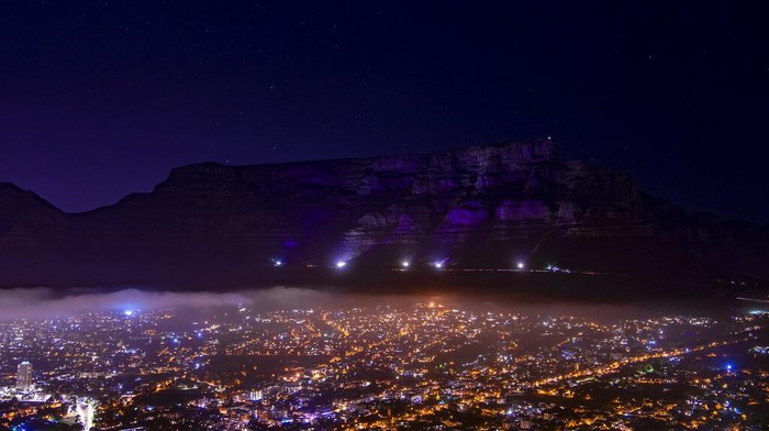 Duka Afrika Selatan Atas Kepergian Desmond Tutu Table Mountain di Cape Town, Afrika Selatan menyala dengan warna ungu pada hari Minggu, 26 Desember 2021, untuk mengenang Uskup Agung Anglikan Desmond Tutu. Presiden Afrika Selatan mengatakan Tutu, aktivis pemenang Hadiah Nobel Perdamaian Afrika Selatan untuk keadilan rasial dan hak-hak LGBT dan pensiunan Uskup Agung Anglikan Cape Town, telah meninggal pada usia 90 tahun. (AP Photo)