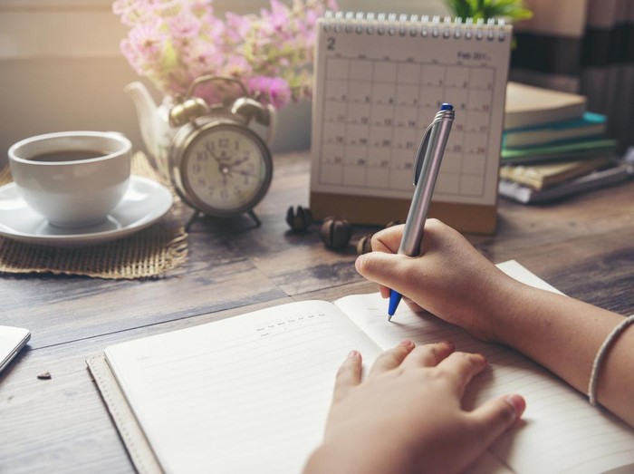 On 2019 Calendar book,Femalehand of planner writing daily appointment.Woman mark and noted schedule(holiday trip) on diary at office desk.Calendar reminder event for planner concept