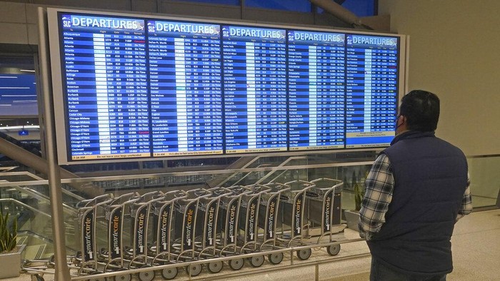 Saat Ratusan Penerbangan Batal Gegara Omicron, Liburan Natal di AS Kacau! Seorang pria melihat papan keberangkatan di Bandara Internasional Salt Lake City Jumat, 24 Desember 2021, di Salt Lake City. Setidaknya tiga maskapai besar mengatakan mereka telah membatalkan lusinan penerbangan karena penyakit yang sebagian besar terkait dengan varian omicron dari COVID-19 telah berdampak pada jumlah awak penerbangan selama musim perjalanan liburan yang sibuk. (Foto AP/Rick Bowmer)