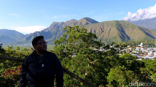 Seorang wisatawan menikmati udara pagi yang segar di atas Bukit Selong dengan latar belakang Bukit Pergasingan yang sebelahnya terlihat juga dengan jelas Gunung Rinjani.