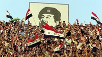 Suporter bola bersorak dengan latar bergambar Saddam Hussein, (17/4/2001) atau sepekan menjelang ulang tahun Saddam. Saddam dieksekusi mati 3 tahun pasca invasi AS ke Irak, 2006. (Photo by Karim Mohsen/Newsmakers)
