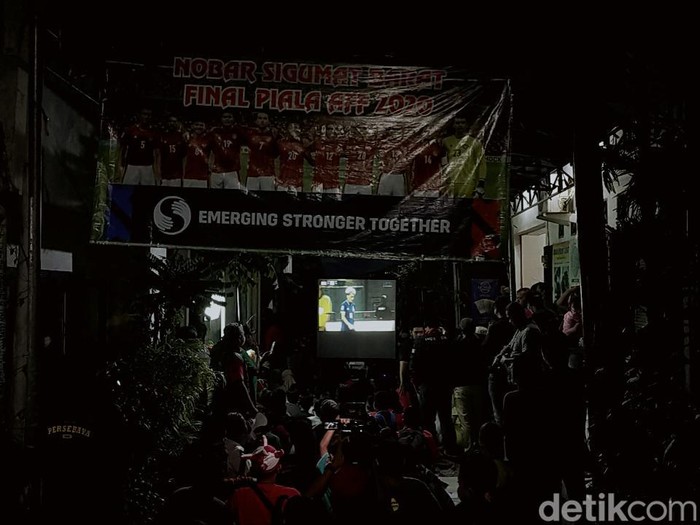 Timnas Indonesia tengah bertanding melawan Thailand dalam laga leg pertama final Piala AFF 2020. Dukungan untuk Timnas bergema di Surabaya.