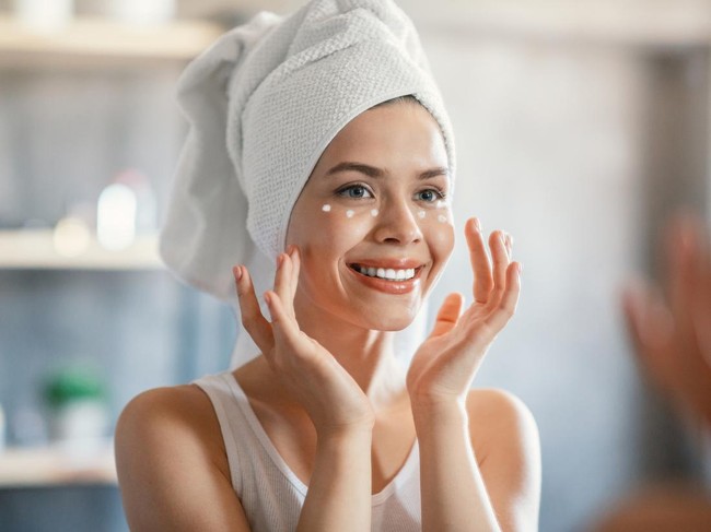 Portrait of lovely lady applying cream under her eyes near mirror indoors.