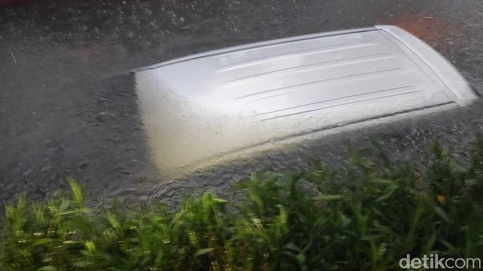 Sebuah mobil nyemplung ke selokan saat hujan deras mendera Surabaya. Pengemudi tak tahu jika yang dilewatinya adalah selokan karena air selokan rata dengan jalan.