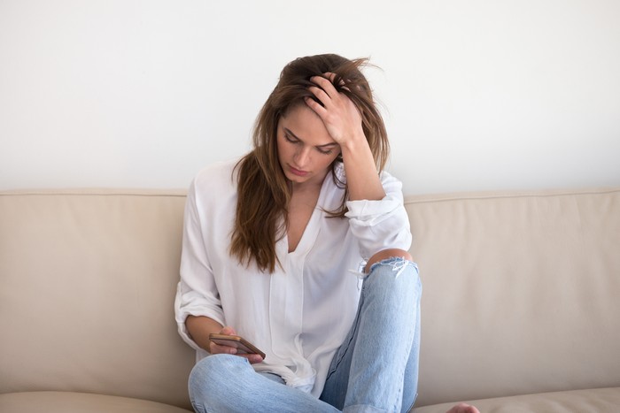 Sad young woman desperately looking at smartphone screen, waiting call from boyfriend or lover, depressed woman holding phone, broken after message received. Concept of loneliness, breaking up