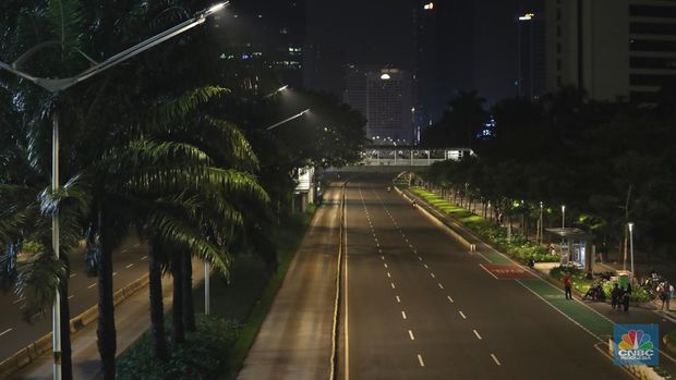 Seorang pedang kopi keliling melewati ruas jalan utama di kawasan jalan Sudirman-Thamrin, Jakarta, Sabtu (1/1/2022). Sejak pukul 22.00 WIB terpantau kendaraan dan warga  sangat lengang. Kendaraan operasional polisi tampak menyusuri ruas-ruas jalan yang menjadi titik penutupan jalan.Malam pergantian tahun 2021 menuju 2022 di pusat Kota Jakarta berlangsung sepi. Pemerintah Provinsi DKI Jakarta bersama Polda Metro Jaya menutup 11 ruas jalan sejak pukul 22.00 WIB.Dari pantauan dilokasi sejumlah ruas jalan di Jakarta terpantau lengang. Tak banyak kendaraan melintas.   Kendaraan operasional polisi tampak menyusuri ruas-ruas jalan yang menjadi titik penutupan jalan (CNBC Indonesia/ Tri Susilo)