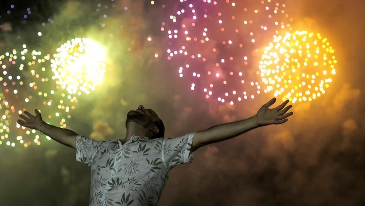 Potret Kemeriahan Tahun Baru di Penjuru Dunia A man celebrates the start of the New Year, backdropped by fireworks exploding in the background over Copacabana Beach in Rio de Janeiro, Brazil, Saturday, Jan. 1, 2022. (AP Photo/Bruna Prado)