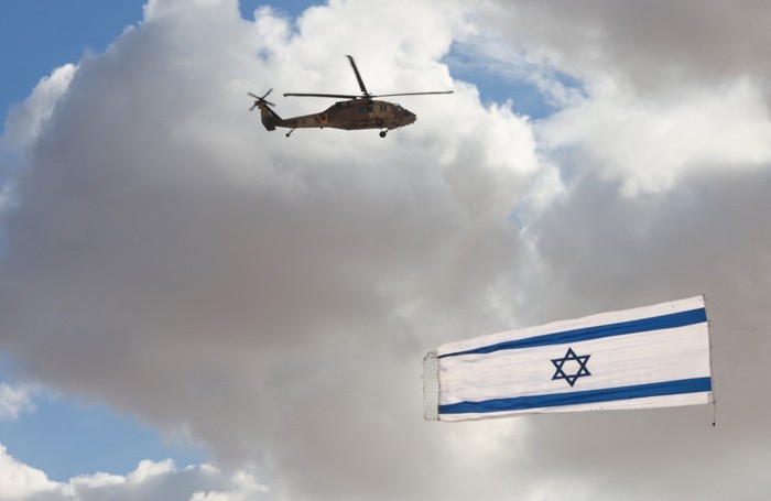 Israeli Blackhawk helicopter perform with flag during an air show as part of a graduation ceremony of Israeli pilots at the Hatzerim air force base in the southern Negev desert, near the city of Beersheva,on December 22, 2021. (Photo by Menahem KAHANA / AFP)