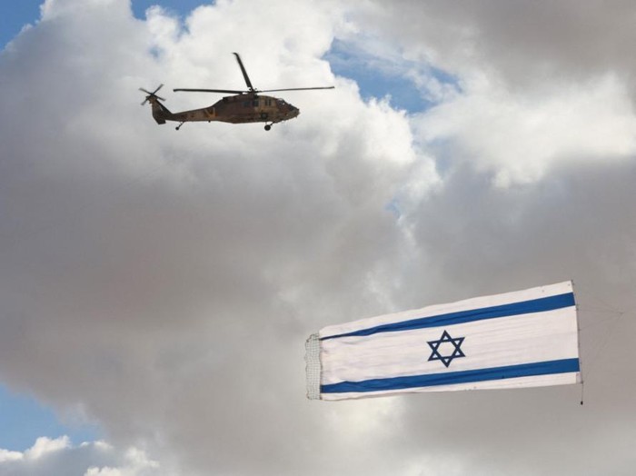 Israeli Blackhawk helicopter perform with flag during an air show as part of a graduation ceremony of Israeli pilots at the Hatzerim air force base in the southern Negev desert, near the city of Beersheva,on December 22, 2021. (Photo by Menahem KAHANA / AFP)