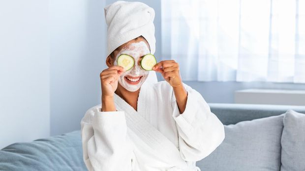 ilustrasi skincare Woman with facial mask and cucumber slices in her hands. Beautiful young woman with facial mask on her face holding slices of fresh cucumber. Young woman with clay facial mask holding cucumber slices