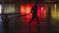 Seorang warga yang mengenakan masker menarik seorang anak melintasi danau beku dekat Olympics Green di Beijing, China. AP/Ng Han Guan.