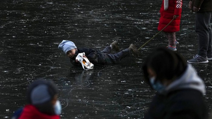 A child falls as residents bring their children to play on a frozen river near a residential area during the New Year holiday in Beijing, Monday, Jan. 3, 2022. (AP Photo/Andy Wong)