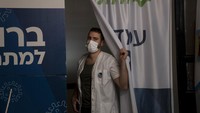 Seorang pekerja medis Clalit Health Services mengintip dari stannya saat dia memanggil pasien berikutnya untuk memberikan vaksin virus Corona di Yerusalem, Senin, (3/1/2022). AP/Maya Alleruzzo.