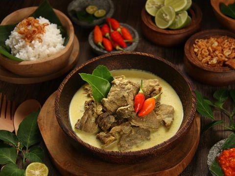 Gulai Kambing, the traditional mutton curry soup  popular in Central and East Java. Mutton chunks braised in coconut milk and curry spices. The soup is served in a shallow wooden bowl. Accompanied with red chili paste and steamed rice.