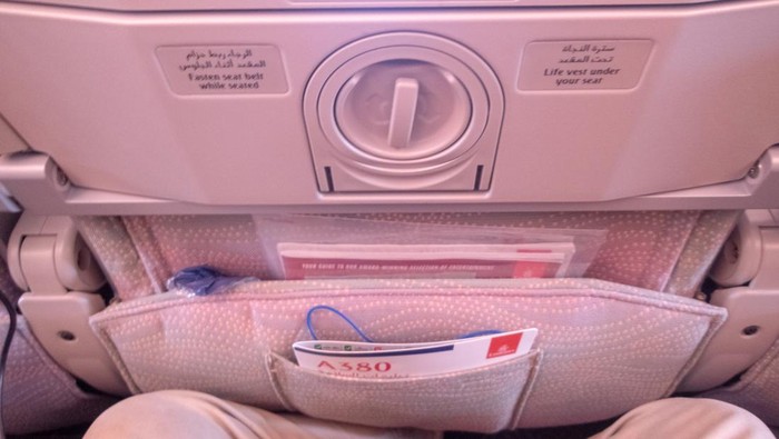Back of the seat on a commercial long haul flight. This is on an Emirates Airbus A380-800 double decker aircraft and shows the safety sheet in the document pocket in the back of the seat with the passengers legs in the shot.