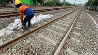 Petugas mengeluarkan batu kerikil dari karung ke lintasan kereta api. Bebatuan kerikil di sekitar bantalan rel kereta api itu memiliki fungsi utama sebagai pemberat. Tujuannya agar posisi rel tetap stabil saat kereta api melintas dalam kondisi cuaca apapun.