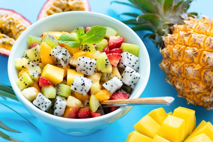Fruit salad in bowl on blue background. Exotic tropical fruit salad. Dragon fruit, passion fruit, mango, coconut, strawberry and pineapple salad in a bowl