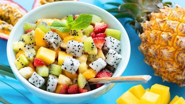 Fruit salad in bowl on blue background. Exotic tropical fruit salad. Dragon fruit, passion fruit, mango, coconut, strawberry and pineapple salad in a bowl