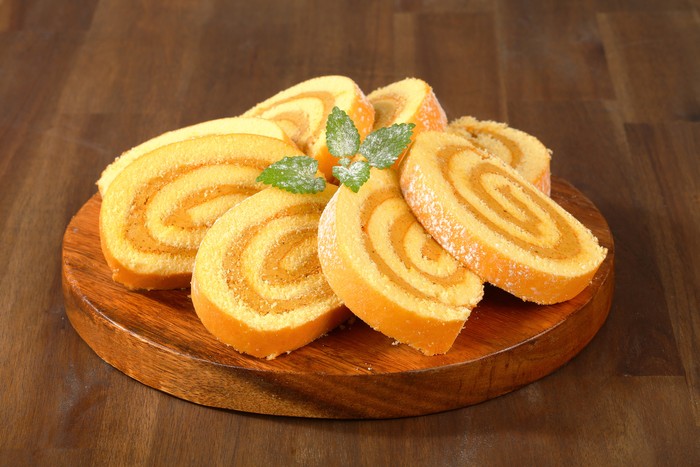 caramel swiss roll slices on a round wooden cutting board