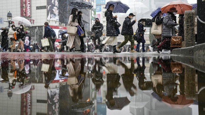 People walk across at the famed Shibuya scramble crossing as the snow comes down Thursday, Jan. 6, 2022, in Tokyo.   Japanese Foreign Minister Yoshimasa Hayashi on Thursday asked that the U.S. military in Japan stay inside its bases to prevent the further spread of COVID-19. Prime Minister Fumio Kishida said he has decided to tighten virus restrictions in Okinawa, Yamaguchi prefecture, where US bases are located, and Hiroshima.(AP Photo/Kiichiro Sato)