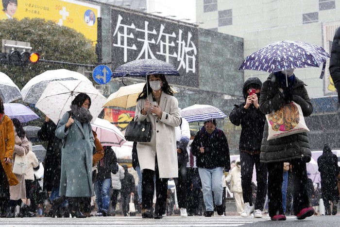 People walk across at the famed Shibuya scramble crossing as the snow comes down Thursday, Jan. 6, 2022, in Tokyo.   Japanese Foreign Minister Yoshimasa Hayashi on Thursday asked that the U.S. military in Japan stay inside its bases to prevent the further spread of COVID-19. Prime Minister Fumio Kishida said he has decided to tighten virus restrictions in Okinawa, Yamaguchi prefecture, where US bases are located, and Hiroshima.(AP Photo/Kiichiro Sato)