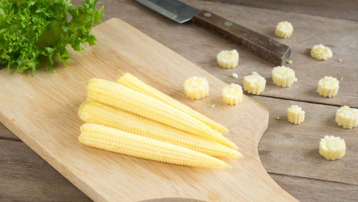 Baby corns and knife on cutting board.