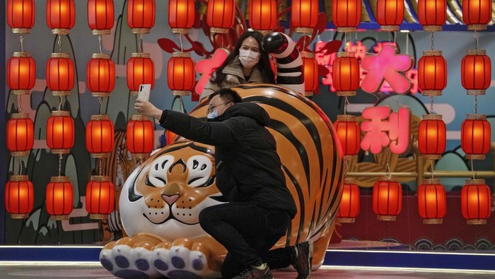 A couple wearing face masks to protect from the coronavirus take a selfie with a tiger decoration, a Chinese zodiac which marks the year 2022, at a shopping mall in Beijing, Sunday, Jan. 9, 2022. Tianjin, a major Chinese port city near the capital Beijing, began mass testing of its 14 million residents on Sunday, after a cluster of a dozen of children and adults tested positive for COVID-19, including a few with the omicron variant. (AP Photo/Andy Wong)