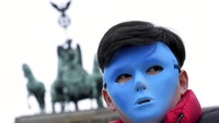Seorang warga mengenakan topeng biru saat berkumpul di depan Gerbang Brandenburg, Berlin, Jerman, Selasa (4/1/2022), untuk melakukan demonstrasi menentang Olimpiade 2022 di Beijing. Dalam demonstrasi tersebut, koalisi organisasi hak asasi manusia menyerukan Menteri Luar Negeri Jerman untuk secara diplomatis memboikot Olimpiade Musim Dingin yang akan digelar di dan sekitar Beijing. AP Photo/Michael Sohn.  