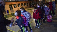 Sekelompok siswa muda yang mengenakan pelindung wajah untuk mencegah penyebaran virus corona, mendisinfeksi tangan mereka sambil menunggu dalam antrean sebelum memasuki sekolah Luis Amigo setelah liburan Natal, di Pamplona, Spanyol utara, Senin, (10/1/2022). (AP/Alvaro Barrientos)
