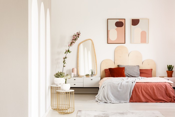 kamar tidur Real photo of a wide bed standing between a shelf with a plant and a shelf with a mirror in a rusty bedroom interior with two posters on a wall and two gold, small tables with plants