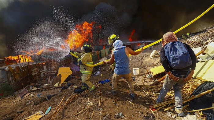 Petugas pemadam kebakaran menunggu air selama kebakaran di lingkungan berpenghasilan rendah Laguna Verde, di Iquique, Chili, Senin, 10 Januari 2022. Menurut pihak berwenang, api menghancurkan hampir 100 rumah di lingkungan yang sebagian besar dihuni oleh migran. (Foto AP/Ignacio Munoz)