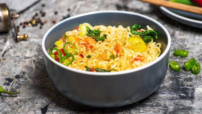 Bowl of cooked instant noodles with spices food ingredients on a grey wooden table tabletop view