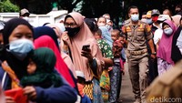 Petugas Satpol PP wara-wiri mengatur barisan warga supaya tidak berdempetan.