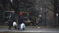 Seorang wanita dan seorang anak laki-laki membawa belanjaan melewati bangkai bus yang terbakar selama bentrokan di Almaty. Kehidupan di Almaty berangsur normal pekan ini. (AP/Vladimir Tretyakov)