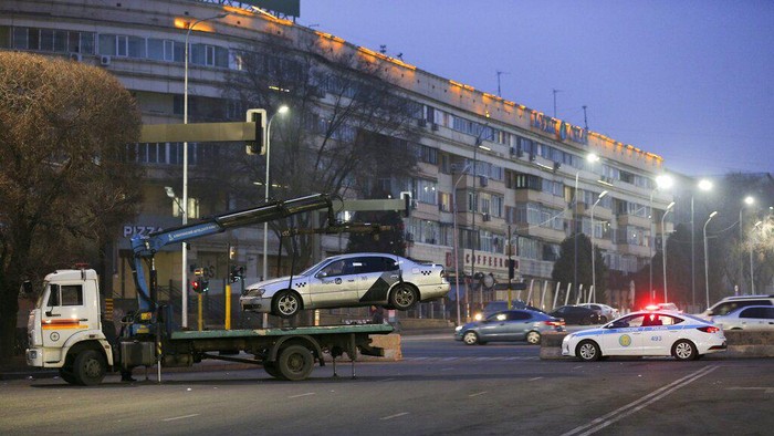 A tow truck transports a car, which was damaged during clashes, from the central square with the city hall in the background in Almaty, Kazakhstan, Tuesday, Jan. 11, 2022. Life in Almaty, which was affected with the violence the most during protests, started returning to normal this week, with public transport resuming operation and malls reopening. (AP Photo/Vasily Krestyaninov)