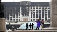 Orang-orang melihat gedung balai kota yang hangus menghitam di alun-alun pusat yang diblokir oleh pasukan dan polisi Kazakhstan di Almaty. (AP Photo)